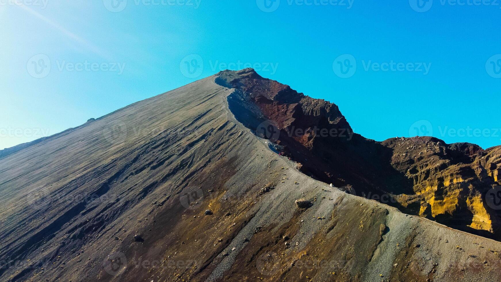 An aerial from the summit of Rinjani shows the stunning Segara Anak Lake below. Surrounded by vibrant blue skies and clouds, the lake's serene beauty stands out against the dramatic landscape. photo