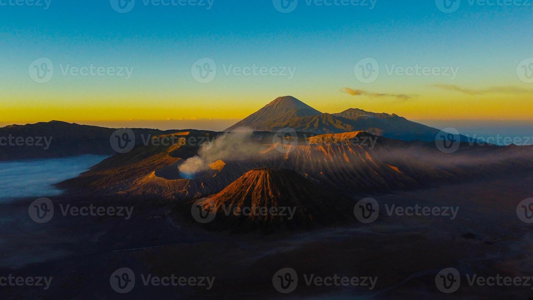 A stunning sunrise at Mount Bromo reveals a vibrant sunset, with clouds gracefully enveloping the peak, showcasing East Java's natural beauty. photo