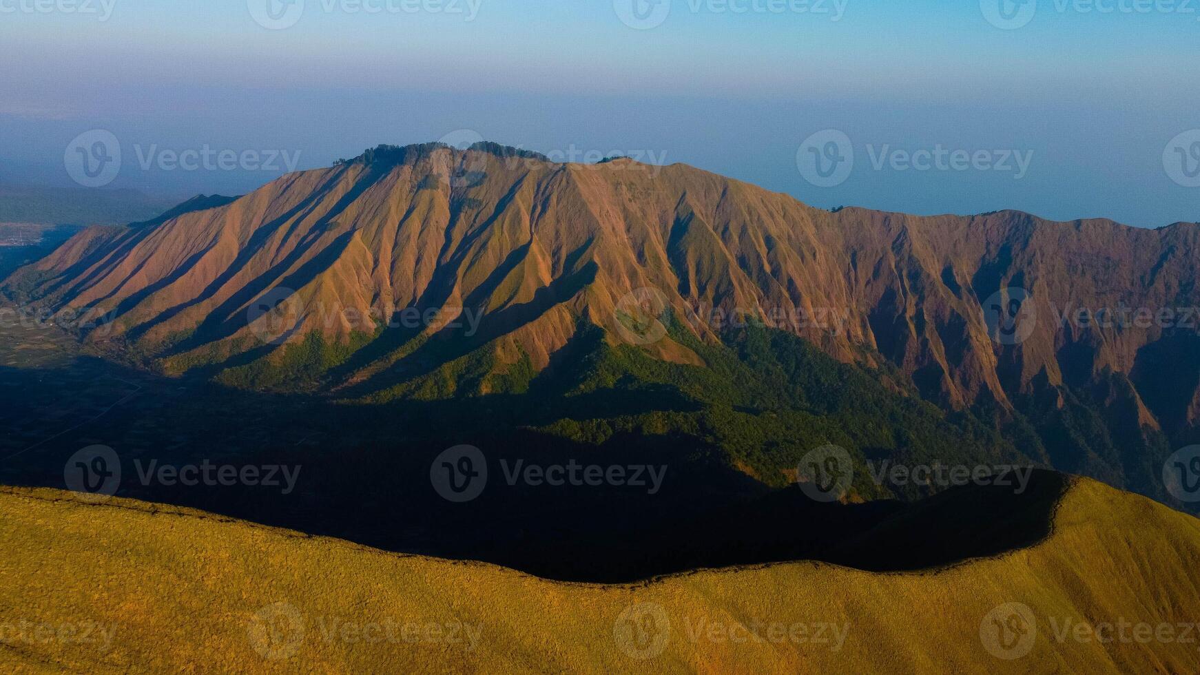 Experience breathtaking aerial views of the rolling hills in Sembalun, at the foot of Mount Rinjani, with expansive savanna turning golden at sunrise. photo