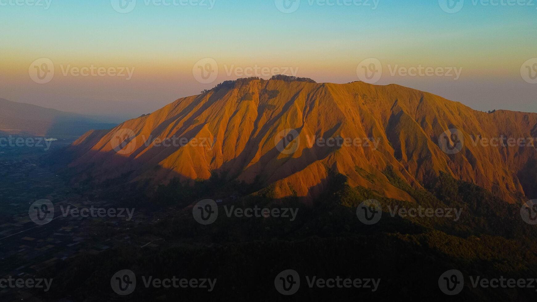 Experience breathtaking aerial views of the rolling hills in Sembalun, at the foot of Mount Rinjani, with expansive savanna turning golden at sunrise. photo