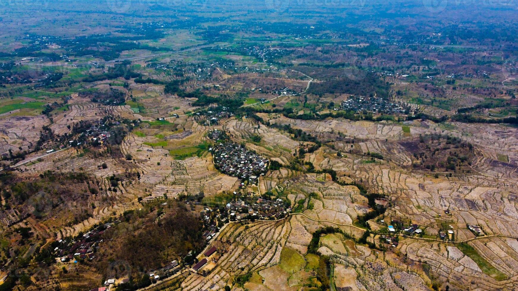 An aerial view of Sade Village in Lombok reveals lush farmland and densely populated homes under the bright midday sun, showcasing vibrant community life. photo