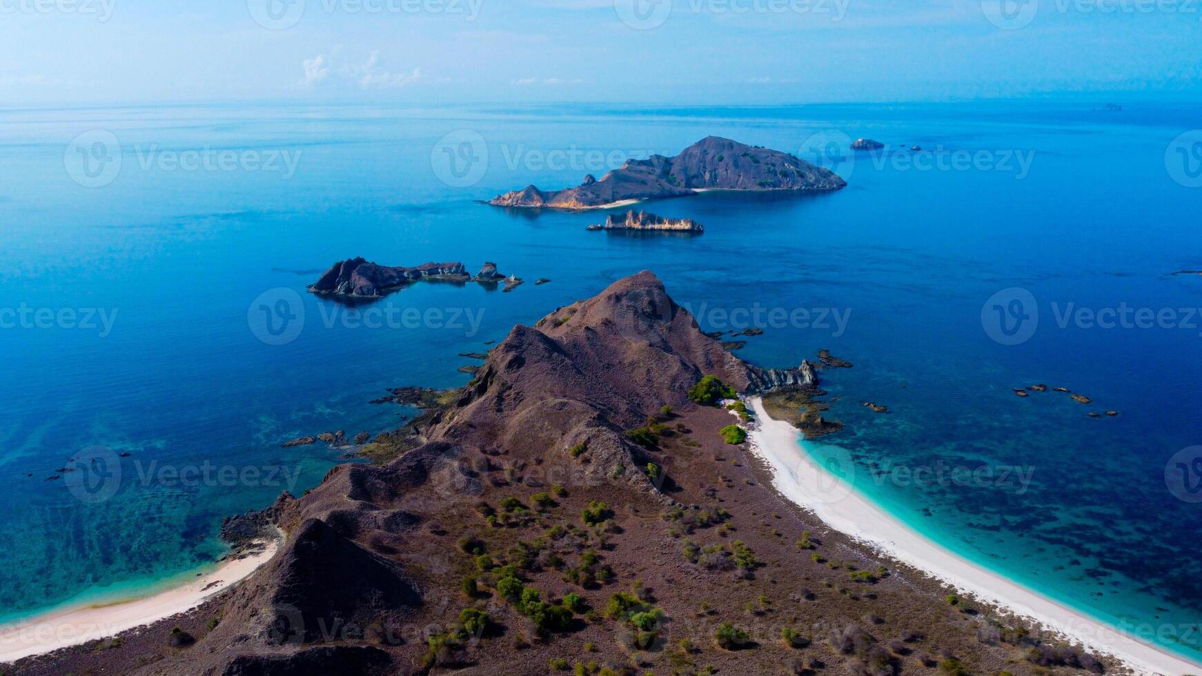 On Padar Island, Pink Beach boasts pristine pink sands and vibrant blue waters, under a clear sky, offering a serene escape with no other visitors. photo