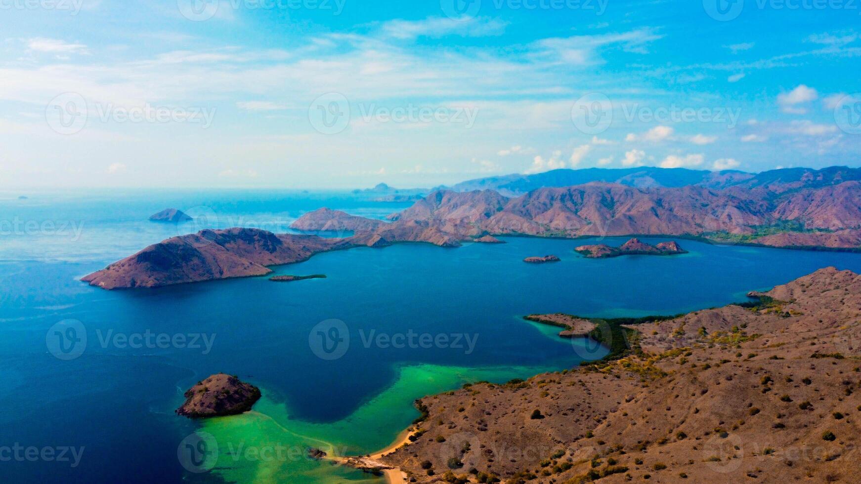 In Kampung Komodo, Indonesia, vibrant blue waters stretch out beneath a clear sky. The serene village backdrop contrasts with the stunning, rich blue of the sea photo