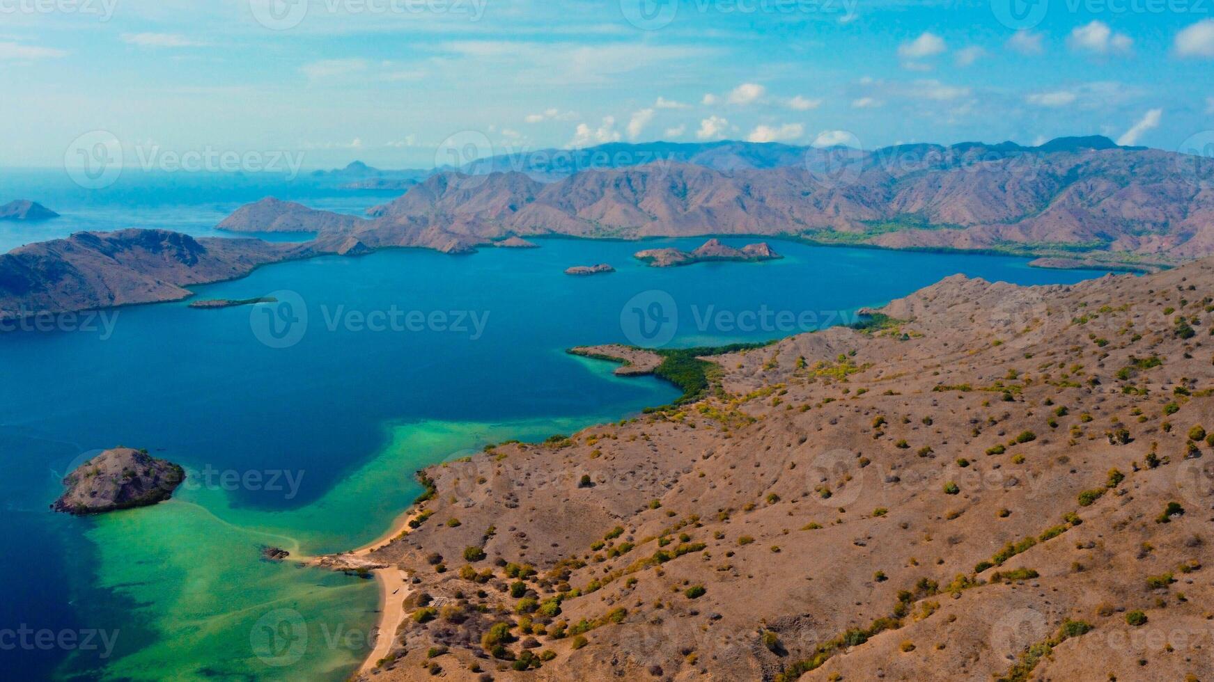 In Kampung Komodo, Indonesia, vibrant blue waters stretch out beneath a clear sky. The serene village backdrop contrasts with the stunning, rich blue of the sea photo