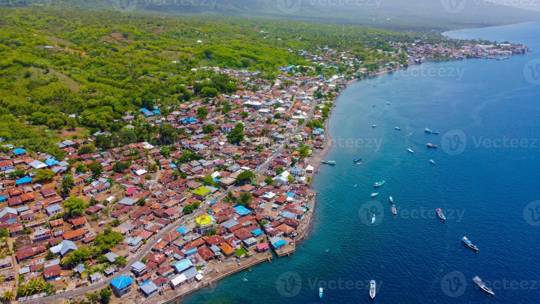 Aerial view of Labuan Bajo harbor at sunset, showcasing numerous pinisi boats docked, with charming local residences surrounding the vibrant scene. photo
