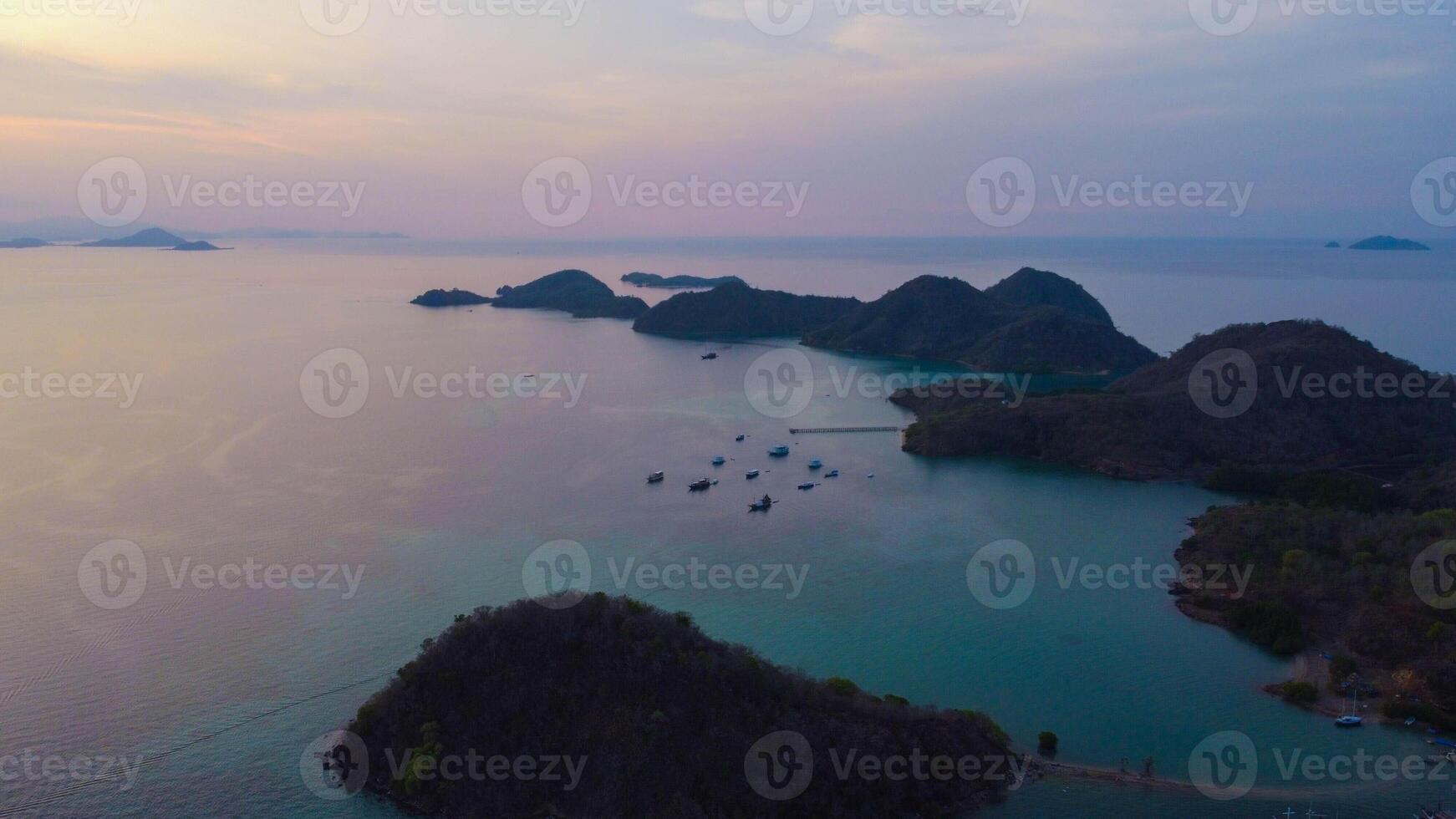 Aerial view of Labuan Bajo harbor at sunset, showcasing numerous pinisi boats docked, with charming local residences surrounding the vibrant scene. photo