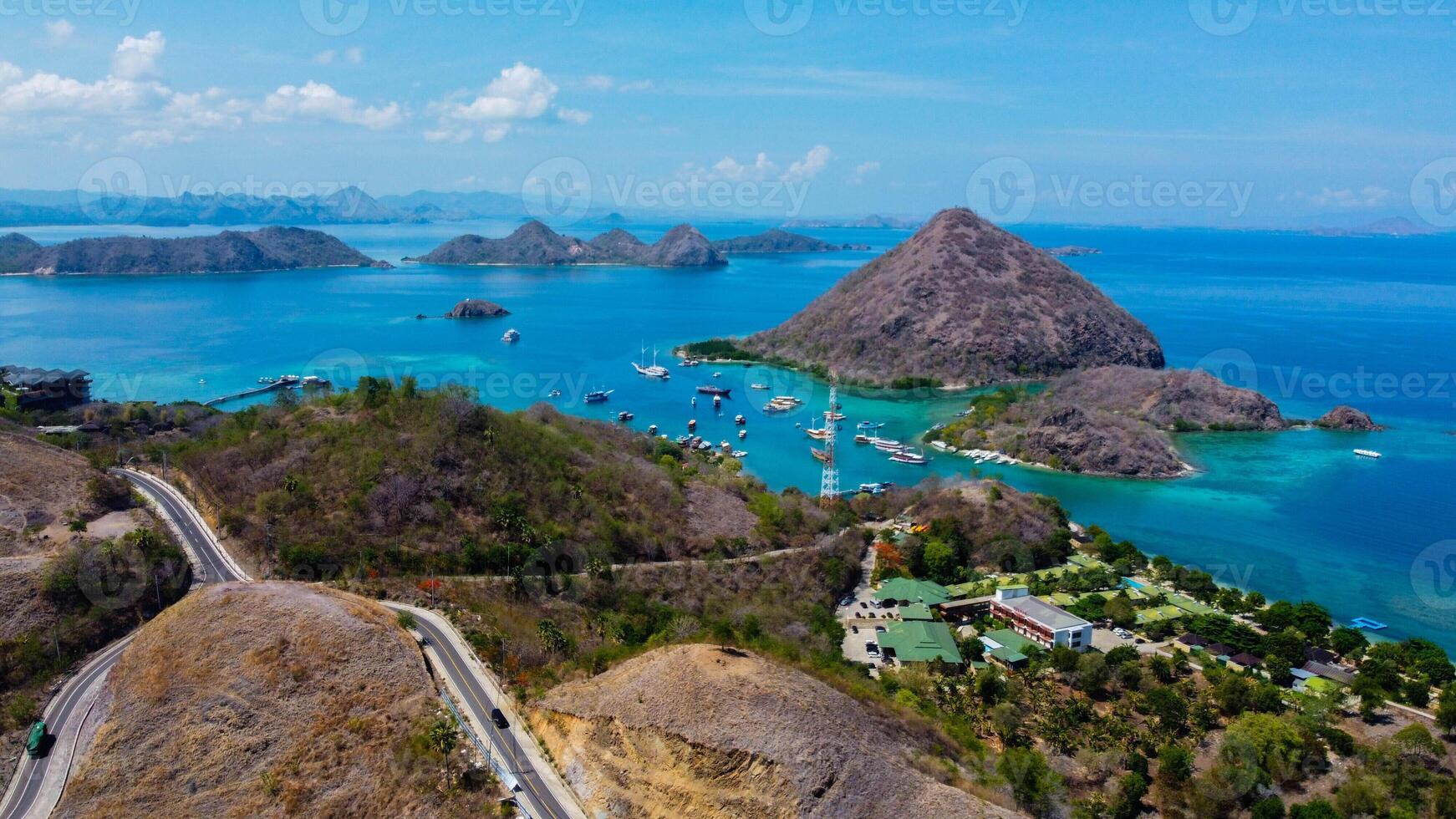 Aerial view of Labuan Bajo harbor at sunset, showcasing numerous pinisi boats docked, with charming local residences surrounding the vibrant scene. photo