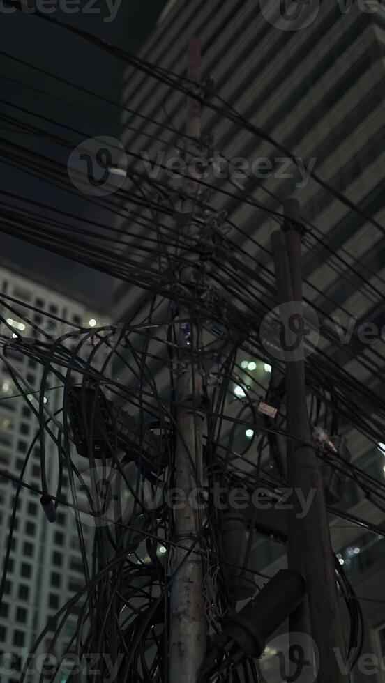 A chaotic bundle of tangled power cables and electrical connections on a utility pole in a densely populated urban area. photo