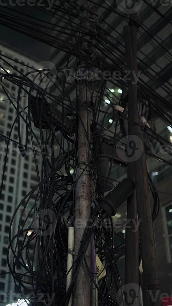 A chaotic bundle of tangled power cables and electrical connections on a utility pole in a densely populated urban area. photo