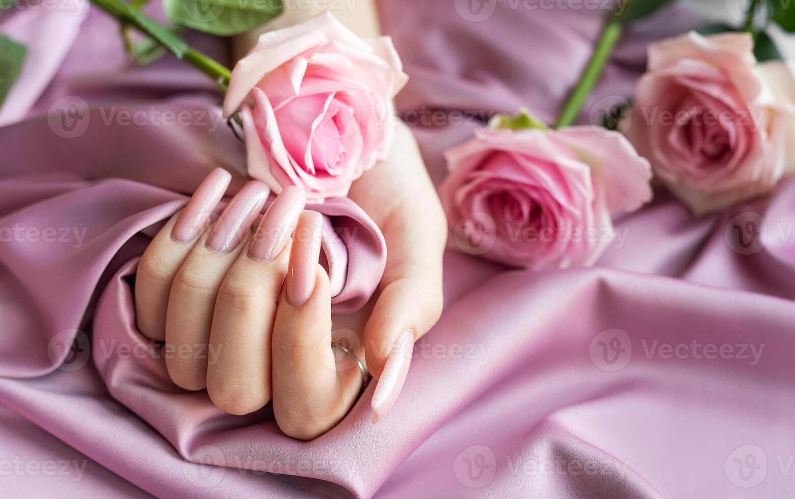 Woman showing pink manicure holding pink rose on pink silk background photo
