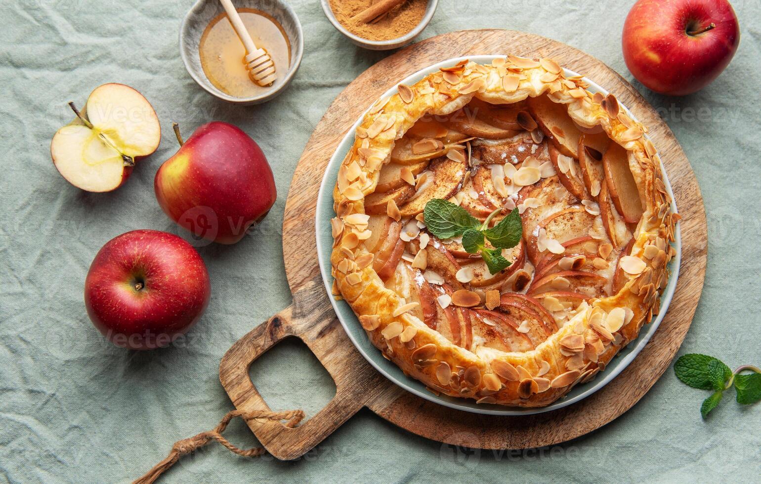 Delicious homemade apple tart displayed on a wooden board surrounded by fresh apples and honey photo