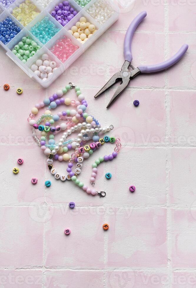 Colorful beads and jewelry making tools arranged on pink tile surface photo