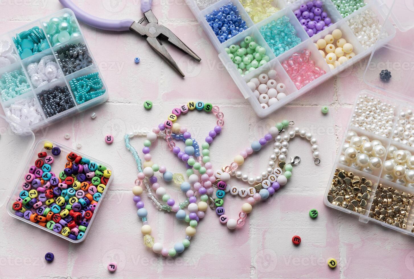 Colorful beads and jewelry making tools arranged on pink tile surface photo