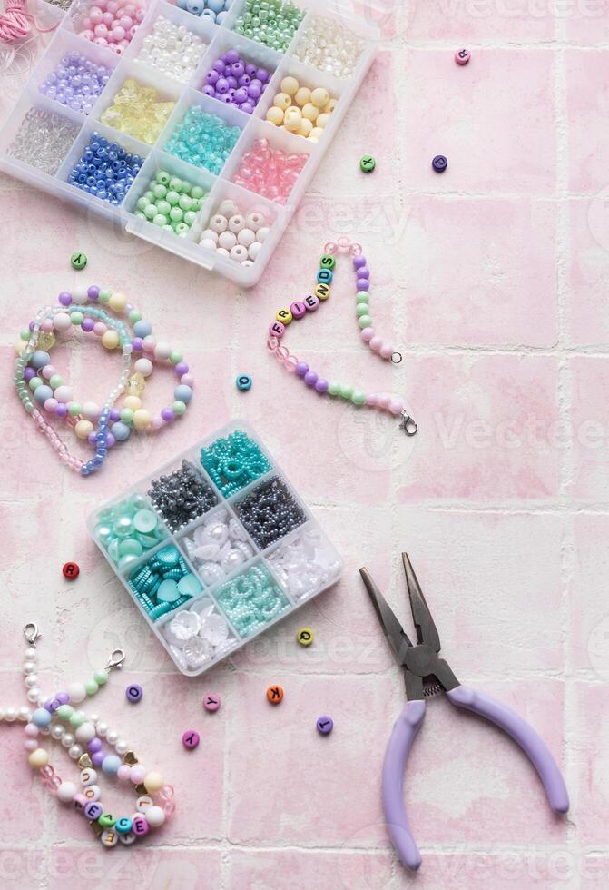 Colorful beads and jewelry making tools arranged on pink tile surface photo