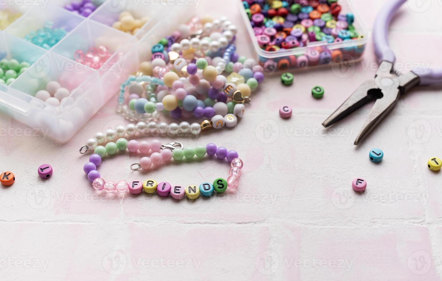 Colorful beads and pliers arranged on pink tile for jewelry making photo