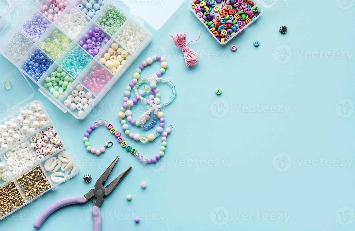Crafting colorful beaded jewelry on a blue surface with tools and a variety of beads photo