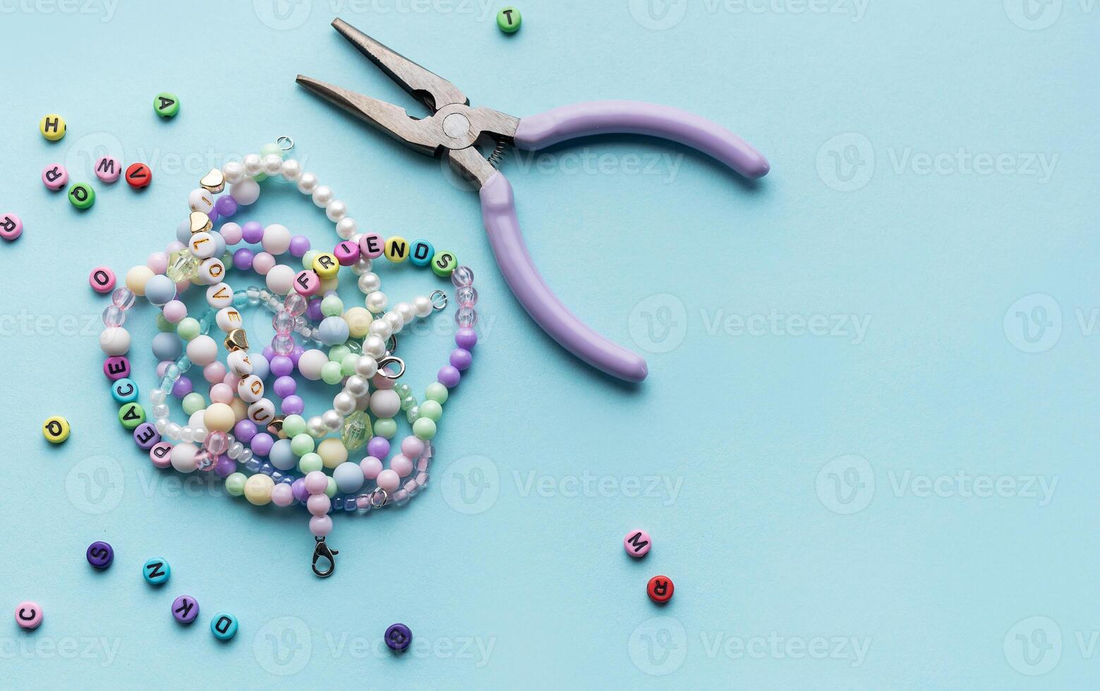 Colorful assortment of beads and jewelry-making tools on a blue surface with completed bracelets photo