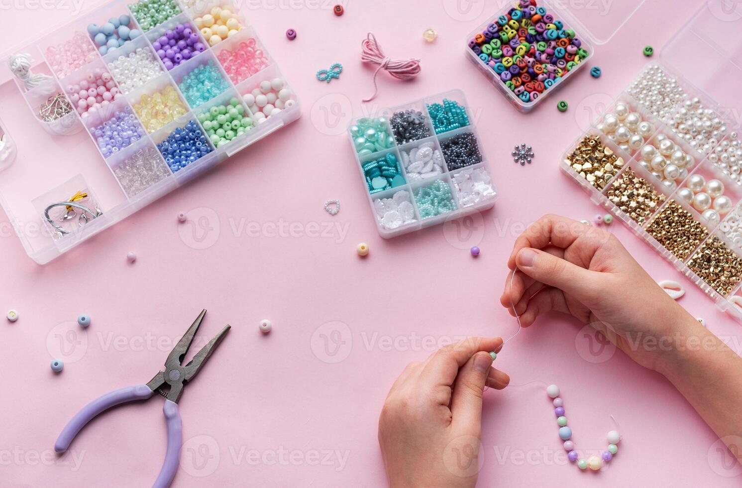 Creating colorful beaded jewelry with assorted beads and crafting tools on a light pink surface photo