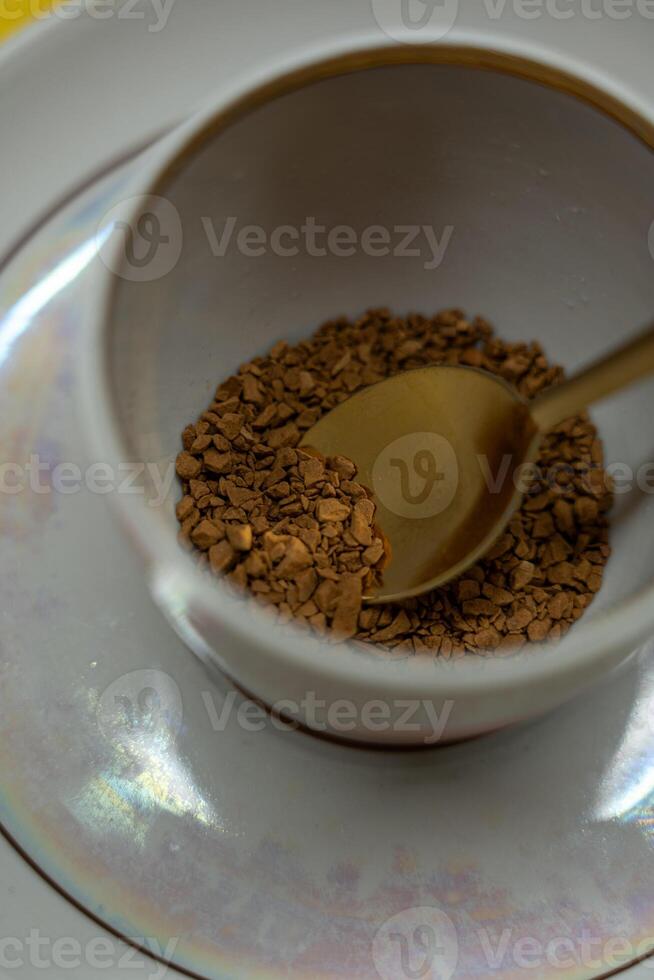 A spoonful of coffee in a mug on a saucer on a yellow background. Close up photo