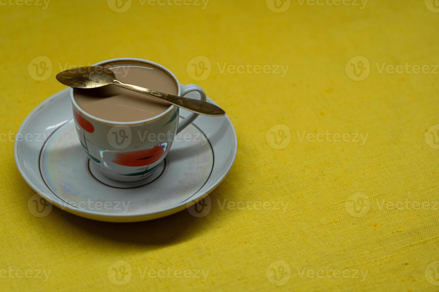 A golden spoon with coffee. Mug in a saucer on a yellow background. Coffee time photo