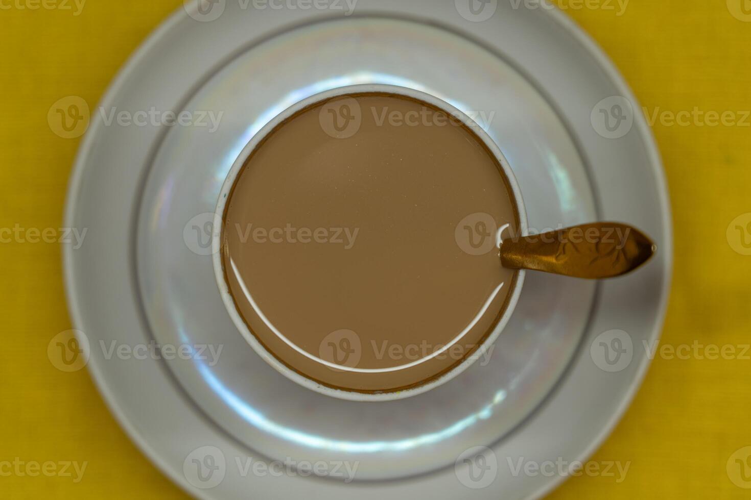 A spoon in a mug with coffee and milk. A mug in a saucer on a yellow background photo