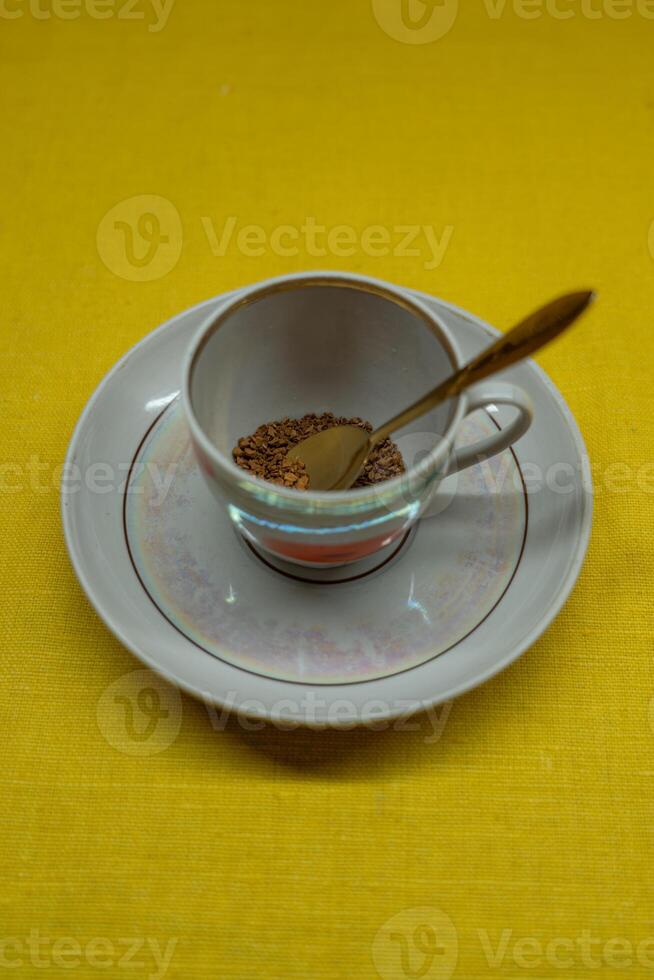 A spoon in a coffee mug on a saucer on a yellow background. Coffee time photo