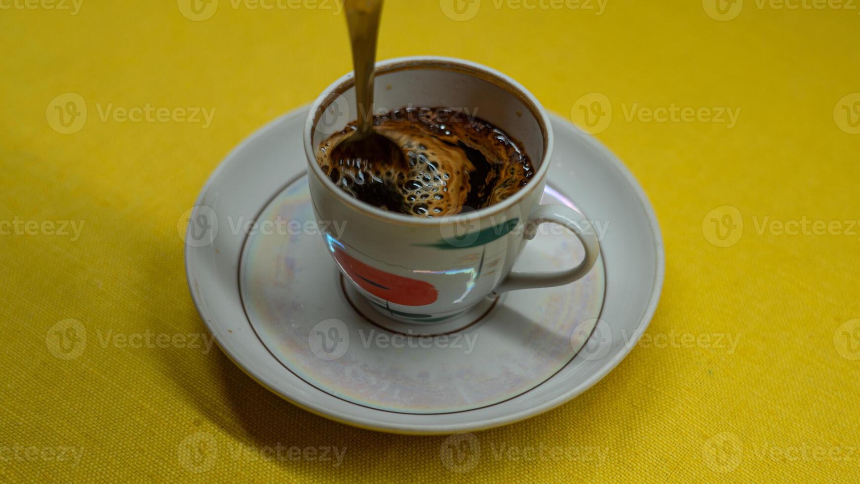 Stirring coffee with a spoon in a mug. A mug in a saucer on a yellow background photo