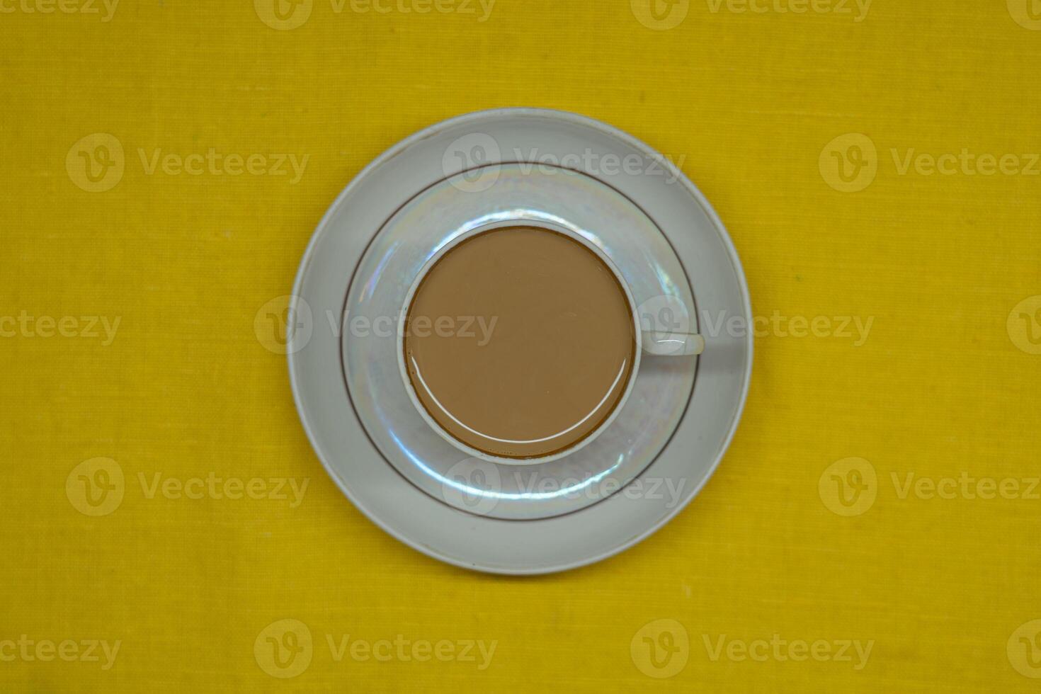 A mug of coffee with milk. Mug in a saucer on a yellow background. Top-down view photo