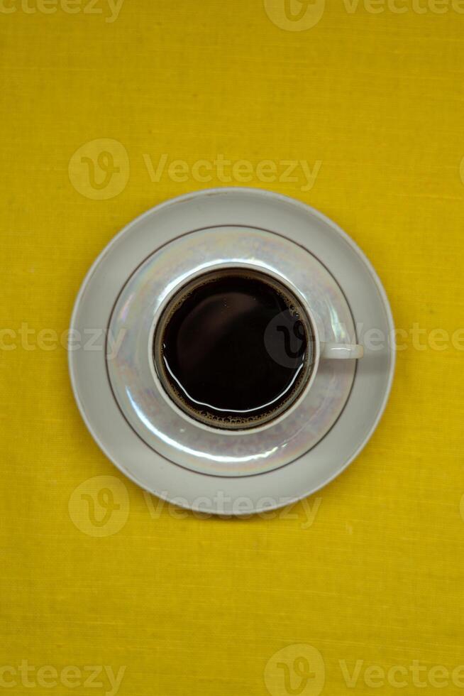 Instant coffee in a mug. A mug in a saucer on a yellow background. Top-down view photo
