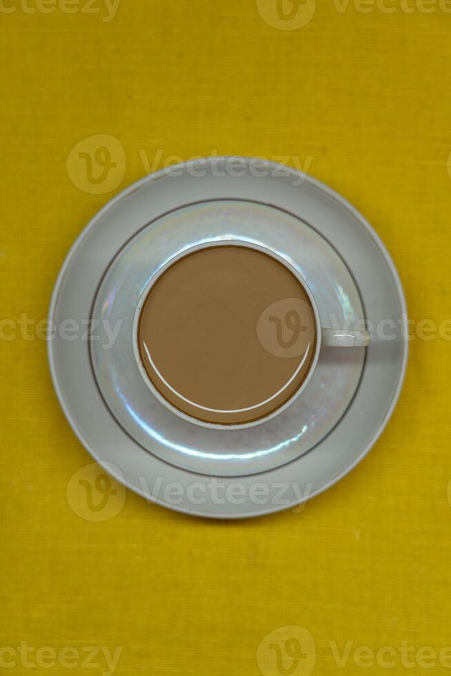 A mug of coffee with milk. Mug in a saucer on a yellow background. Top-down view photo