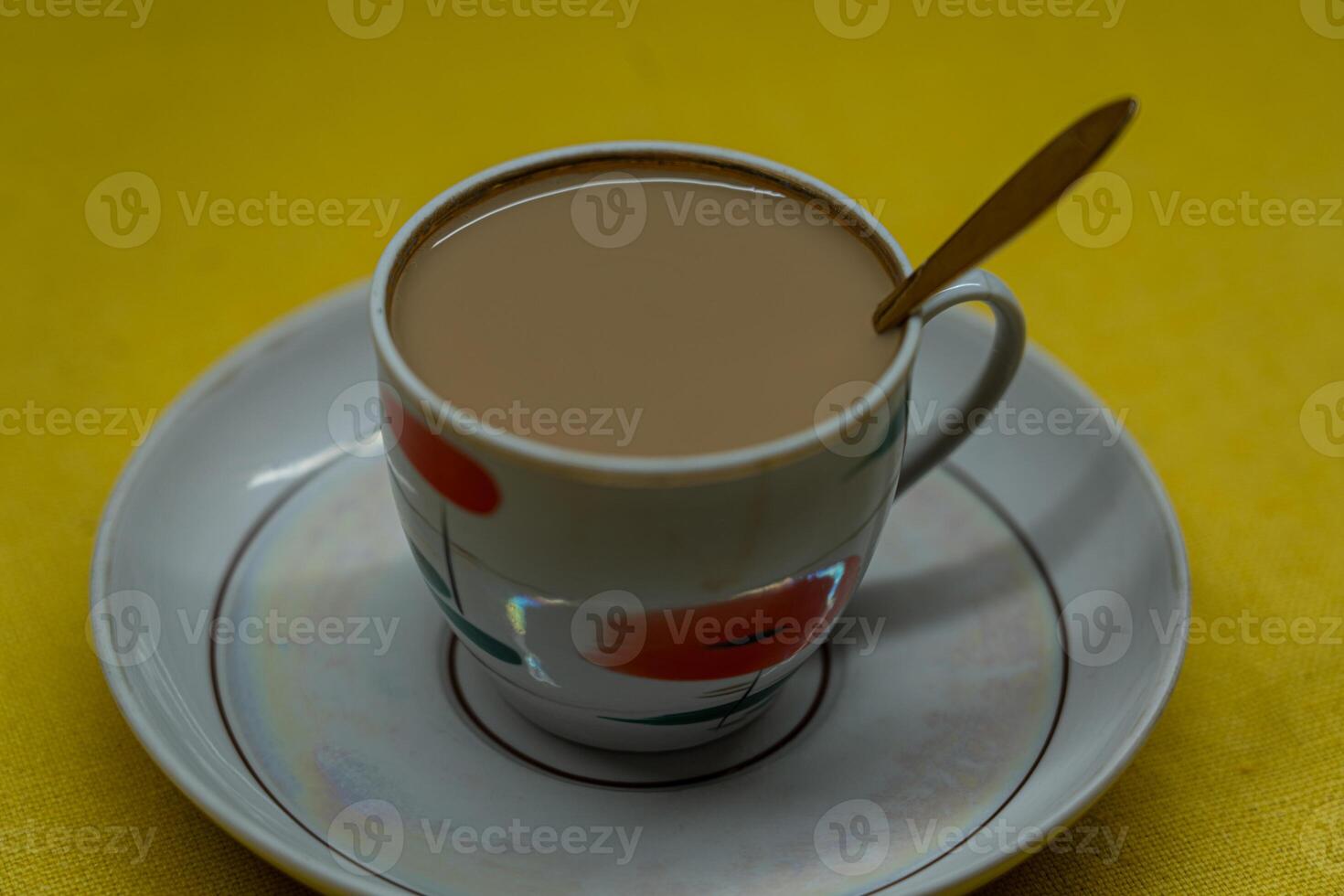 A spoon in a mug with coffee and milk. A mug in a saucer on a yellow background photo