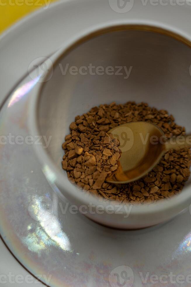 A spoonful of coffee in a mug on a saucer on a yellow background. Close up photo