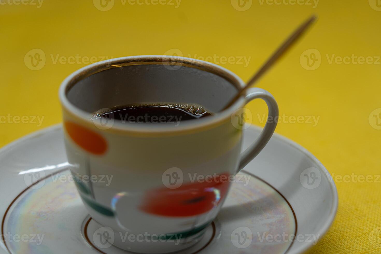 A golden spoon in a coffee mug. A mug in a saucer on a yellow background photo