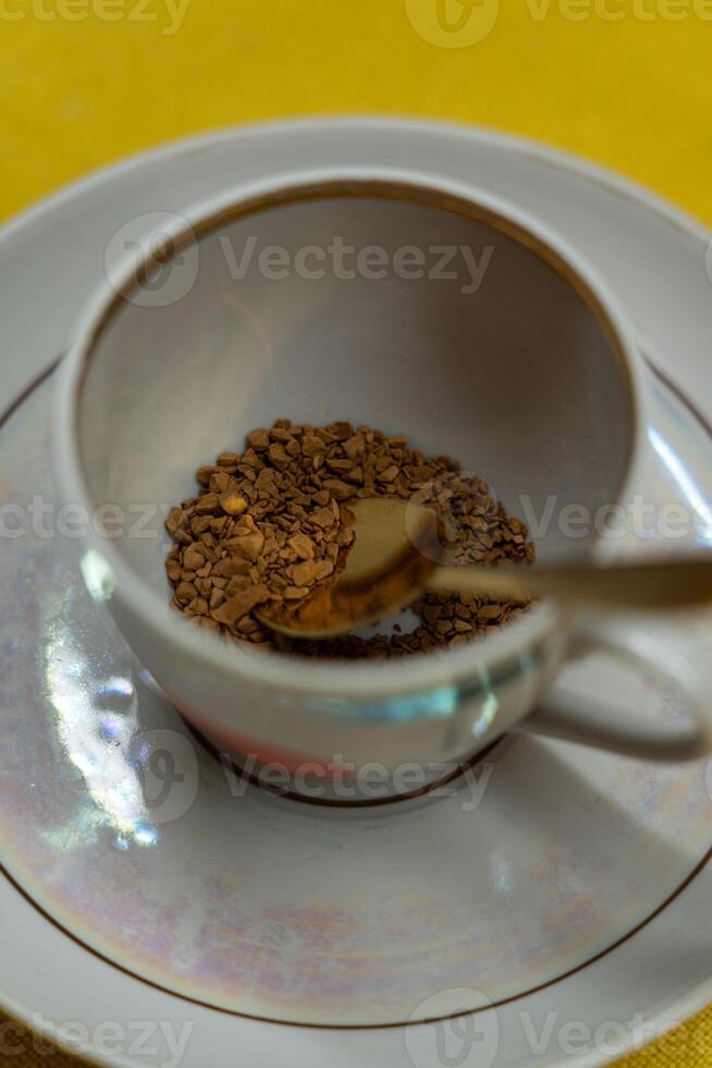 A spoonful of coffee in a mug on a saucer on a yellow background. Close up photo