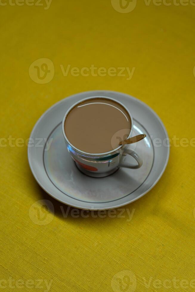 A spoon in a mug with coffee and milk. A mug in a saucer on a yellow background photo