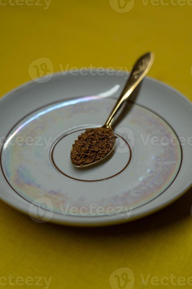 A spoon filled with coffee lies on a saucer on a yellow background. Coffee time photo