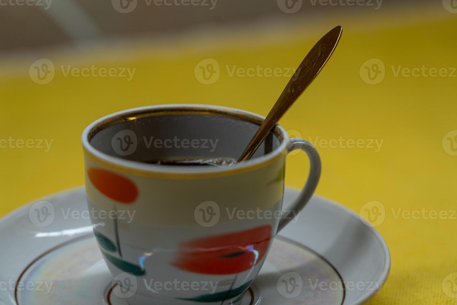 A golden spoon in a coffee mug. A mug in a saucer on a yellow background photo