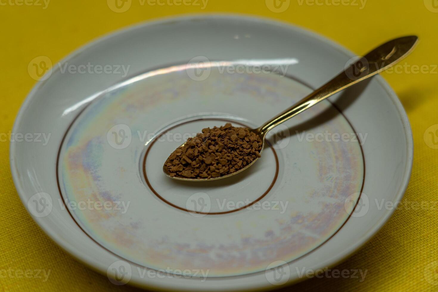 A spoon filled with coffee lies on a saucer on a yellow background. Coffee time photo