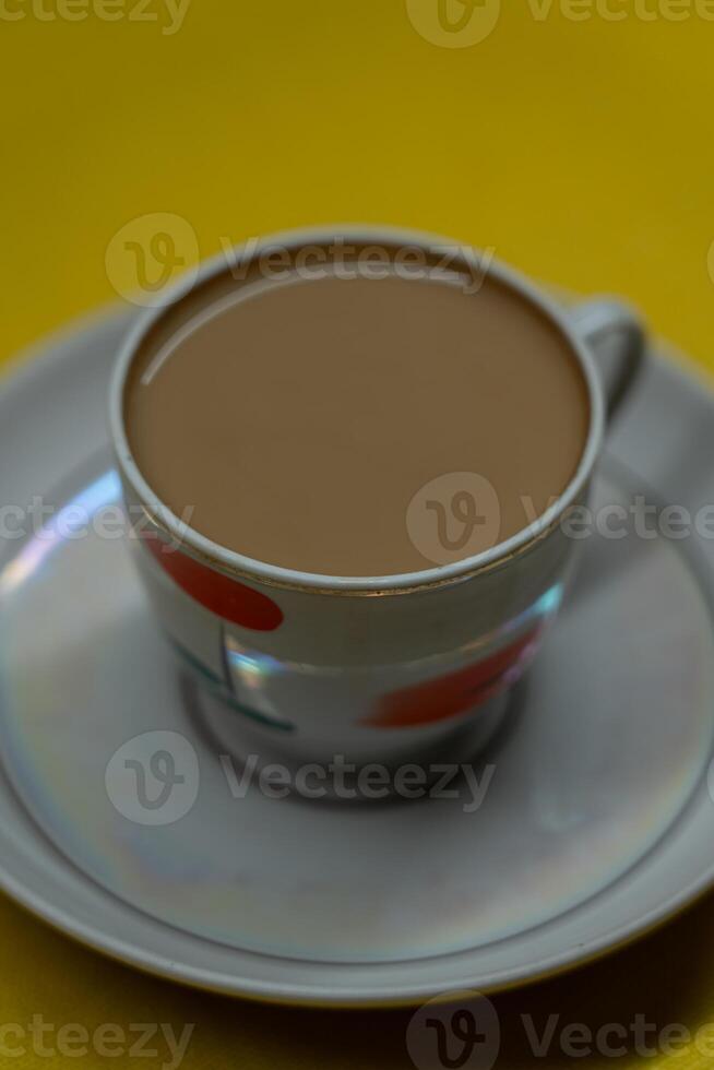 A mug of coffee with milk. Mug in a saucer on a yellow background. Top-down view photo