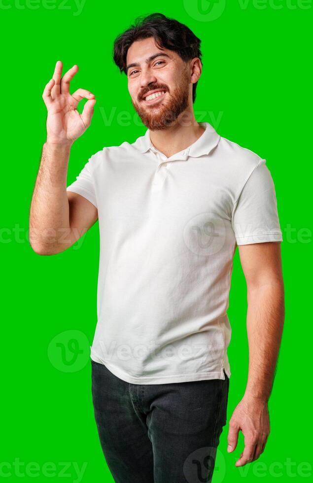 A smiling man in a white polo shirt makes an okay gesture against a bright green background photo
