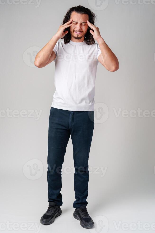 A young man with curly hair rubs his forehead in a casual indoor setting while expressing frustration photo