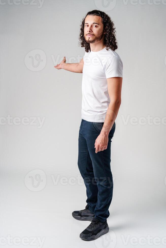 Young man in a white t-shirt and jeans pointing confidently while smiling in a studio setting photo