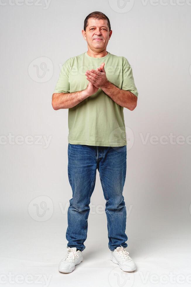 Elderly man claps his hands while standing against a neutral background in a casual light green shirt photo