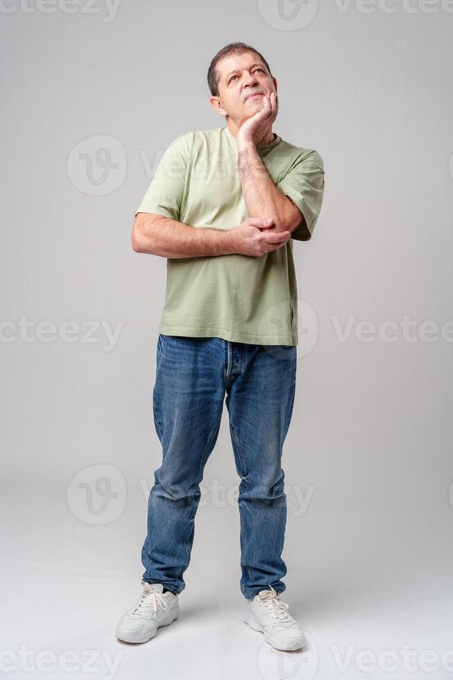 A thoughtful older man expresses gratitude while looking up with hope in a simple green shirt against a light backdrop photo
