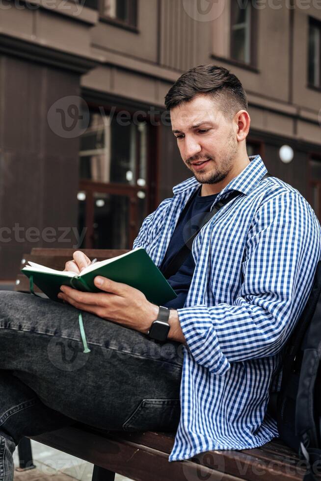 A person writes in a notebook while sitting on a park bench photo