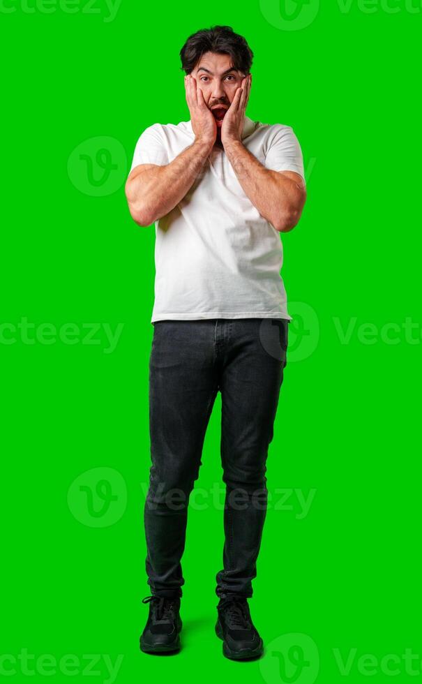 A man with a surprised expression holds his face while against a vibrant green background photo