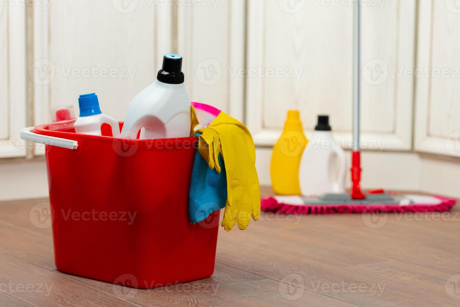 Various household cleaning detergents and bottles in a plastic bucket on the floor photo