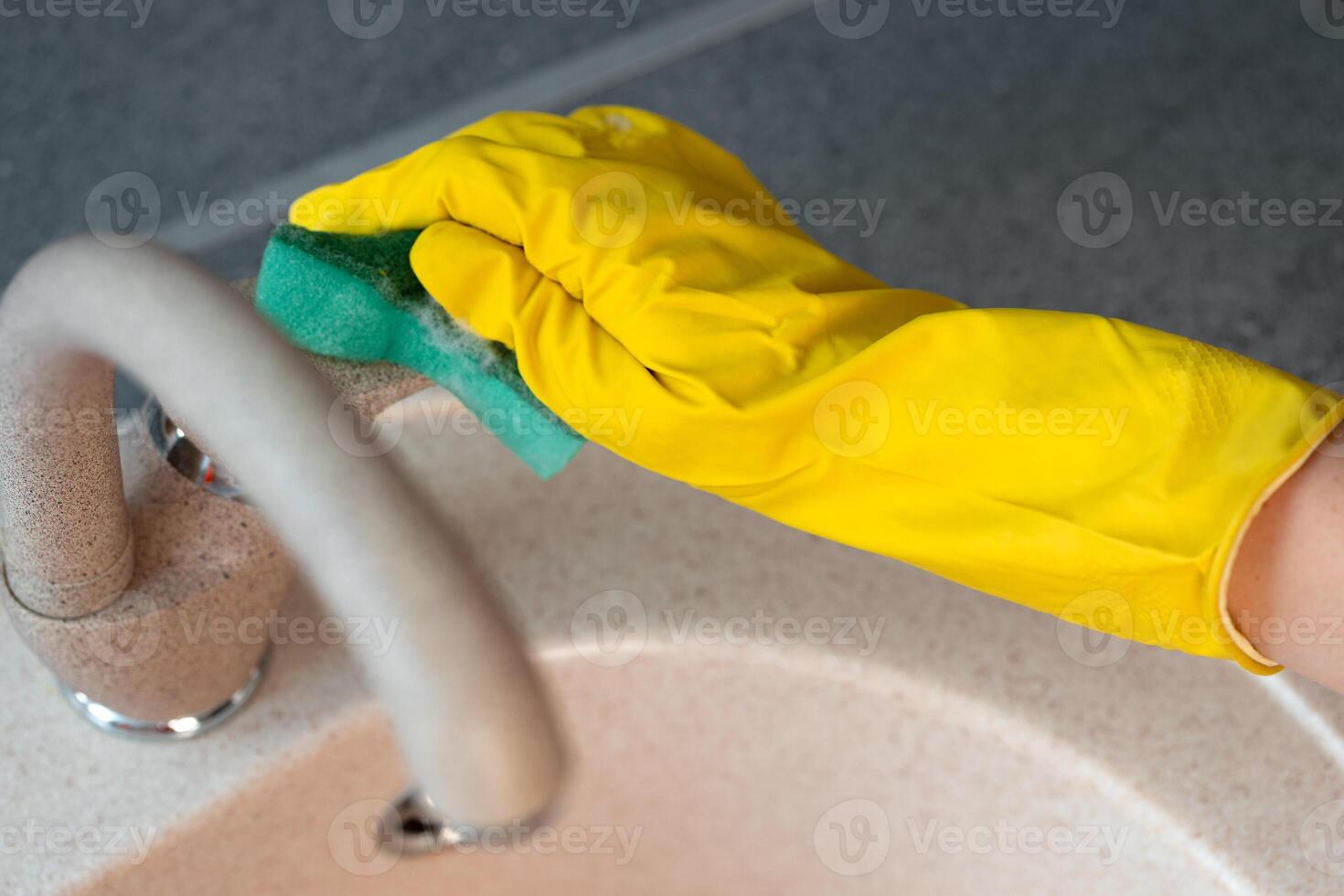 Hands in yellow gloves cleaning a sink with a sponge photo