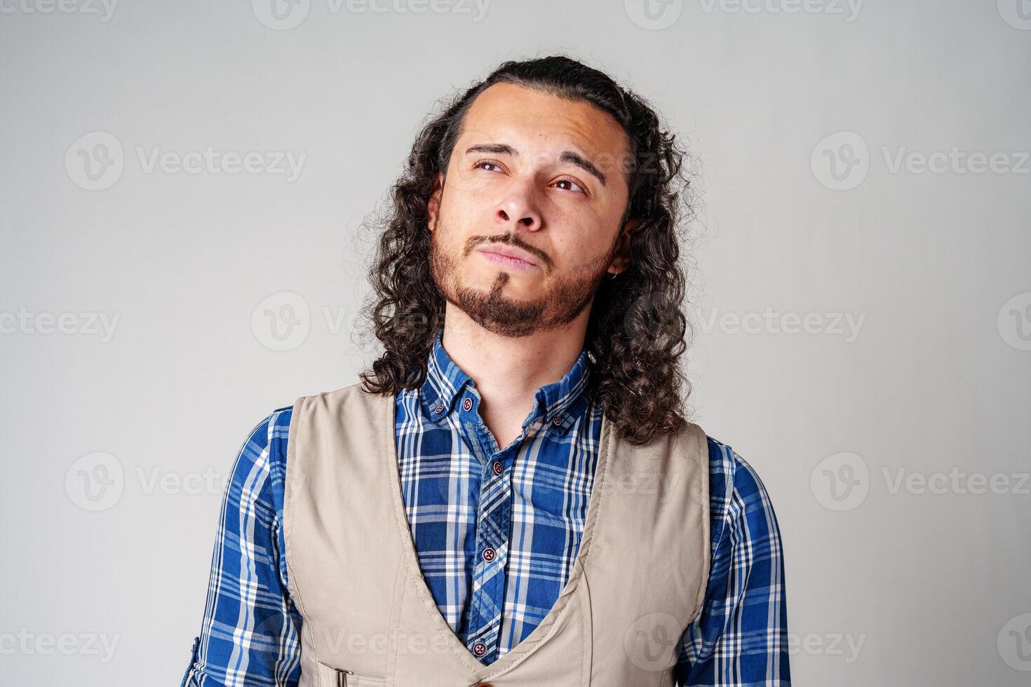 A man with curly hair thoughtfully pondering in a neutral background photo