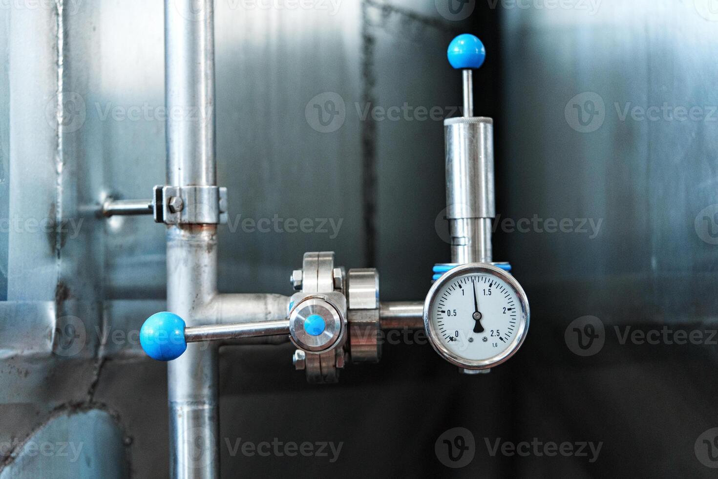 A close-up of a pressure gauge and valve attached to a pipe in a factory setting photo